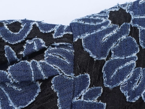 Détail de la broderie florale en denim bleu sur dentelle noire avec bords effilochés