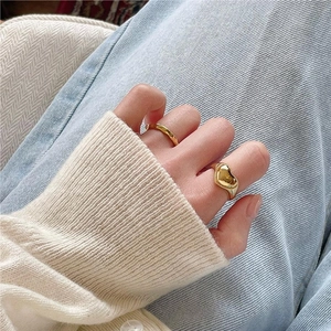 Two golden heart-shaped and wavy rings worn on hand with a soft knit sweater background