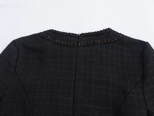 Dettaglio dello scollo dell'abito in tweed nero con elegante catena decorativa dorata
