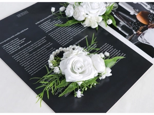Detail of a white silk rose corsage with green leaves and a delicate pearl bead strand