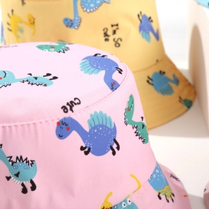 Close-up of pink and yellow sun hats featuring cute cartoon dinosaur prints and fabric texture