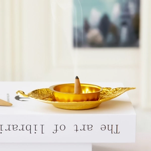 Golden leaf shaped incense burner with smoke rising from cone on white book stand