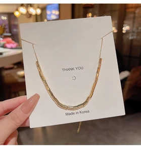 Detail of a minimalist gold bamboo link necklace held on a white thank you display card