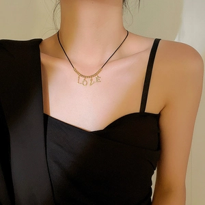 Detail view of gold LOVE pendant with black cord necklace on a female model neck