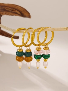 Detail of gold hoop earrings with natural stone and pearl tassels on wooden branch