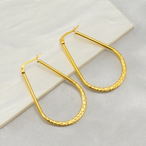 Minimalist gold oval earrings with hammered texture on white marble display