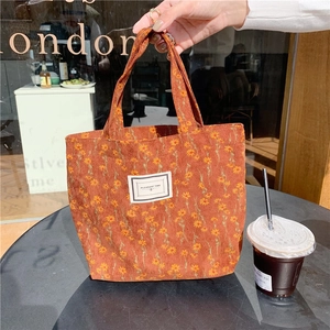 Detail of vintage corduroy floral lunch bag with logo held against a cafe window background