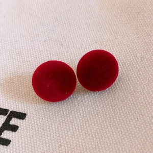 Detail of red velvet spherical stud earrings on a textured light canvas background