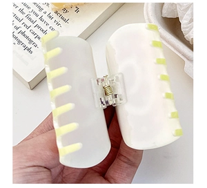 Detail of hand holding a white and yellow striped acrylic shark hair claw clip
