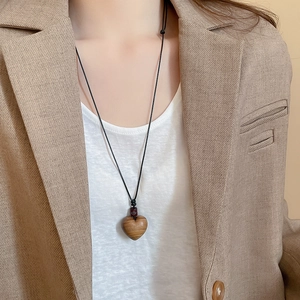 Detail of wooden heart pendant on a black cord necklace worn by a model in a suit