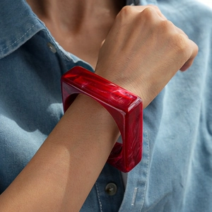 Close-up of a ruby red marble texture resin square bangle worn on a denim shirt