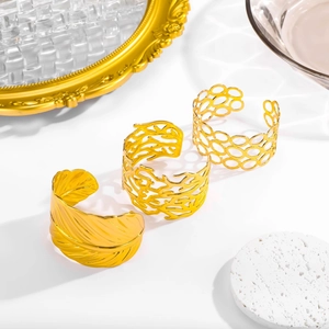 Three gold hollow open cuffs with feather, coral, and honeycomb textures on a mirror