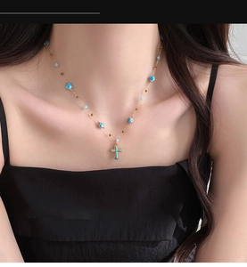 Detail showing bohemian gold cross necklace with blue beads worn on model's neck