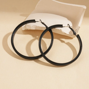 Macro shot of large black matte leather geometric hoop earrings on a textured stone block
