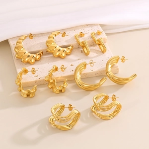 Chunky gold C-shaped and textured hoop earrings on beige stone for a vintage look