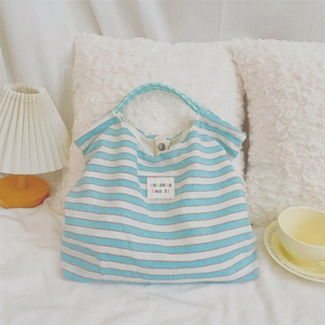 Detail of blue striped canvas tote showing button closure and fabric label on white bedding