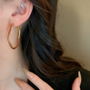 Close-up of a gold twisted hoop earring worn by a model in a warm setting