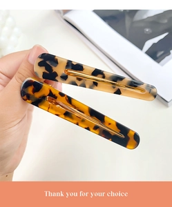 Detail view of two amber leopard print acetate hair clips with golden metal structures