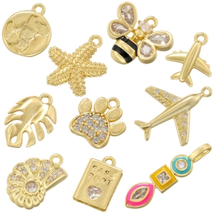 Flat lay of ten gold charms including airplane, palm leaf, starfish and shell with zircon