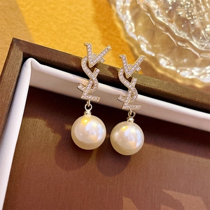 Détail de boucles d'oreilles perles avec logo en lettres et cristaux dans l'écrin