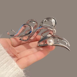 Close-up of elegant silver hollow wave hair claw with white pearl detail held by hand