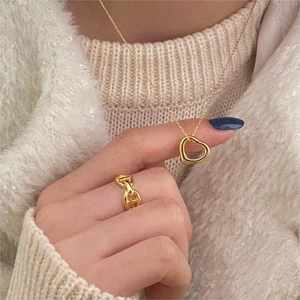 Close-up of golden hollow heart necklace and classic link ring on knit sweater
