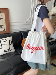 Minimalist white canvas drawstring tote bag with red Bonjour print shown on a model