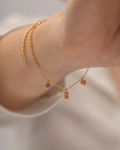 Gros plan d'un bracelet double en or orné de cristaux roses et d'un pendentif rectangulaire