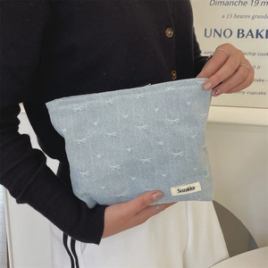 Detail of light blue denim makeup bag with white bow prints and brand woven label