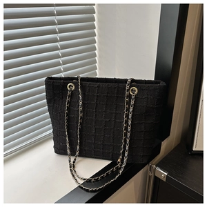 Detail of black tweed tote bag featuring woven plaid texture and golden chain straps