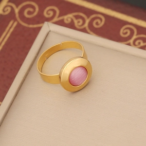 Close-up of golden adjustable ring featuring a round pink cat eye stone on a jewelry box