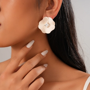 Close-up of a large beige matte flower earring with a square diamond center on a model