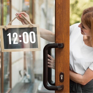 Close-up of wooden hanging chalkboard sign being placed on a glass door by staff