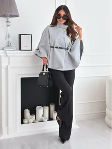 Détail d'un manteau poncho en laine grise avec col montant, bouton doré et ceinture noire