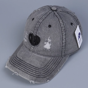 Detail of distressed grey denim baseball cap featuring heart embroidery and frayed edges