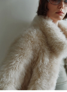 Close-up of cream faux fur vest showing plush curly texture and stand collar detail