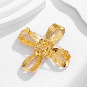 Vintage style gold metal cross bow brooch with textured finish on white background