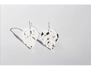 Macro detail of silver monstera leaf earrings with hollow design on white background