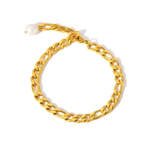 Détail d'une chaîne de cheville gourmette plaquée or ornée d'une perle blanche