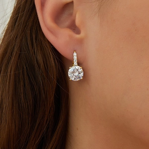 Classic golden hoop earrings with round four-prong zircon stones worn by a model