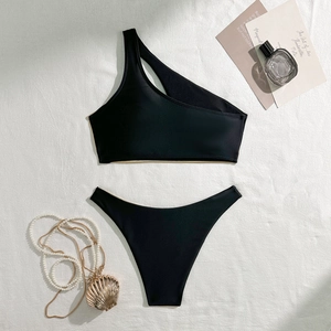 Close-up of a black one-shoulder bikini with gold foil trim and resort accessories