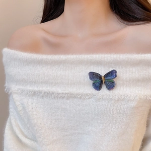 Detailed view of an embroidered butterfly brooch pinned on a white knitted sweater