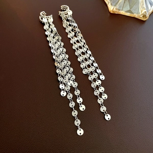 Detail of silver long tassel earrings with metallic sequins on a leather background