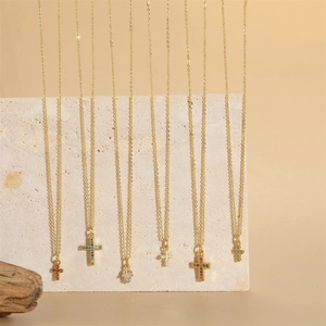 Gold cross and Hamsa hand necklaces with colorful zircon stones on stone background