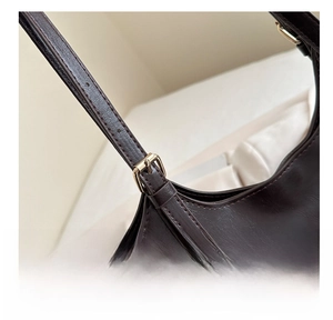 Detail of adjustable golden metal buckle on dark brown polished leather shoulder strap