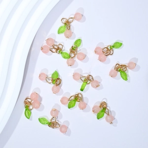 Flat lay of pink cherry pendants with green leaves and gold alloy loops on white background