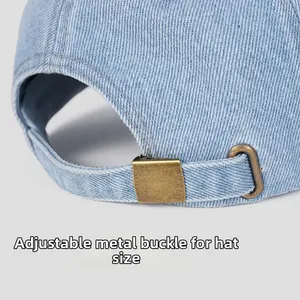 Detailed macro view of the adjustable bronze metal buckle on a light blue denim baseball cap
