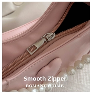 Detailed close-up of smooth silver zipper on pink leather bag with pearl strap accents
