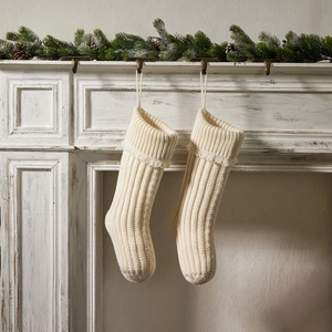 Pair of cream white knitted Christmas stockings hanging on a rustic white mantelpiece decor