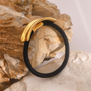 Macro shot of polished gold metal hair cuff with black elastic tie on natural stone